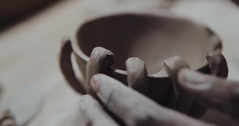 A woman smooths clay as she makes a mug