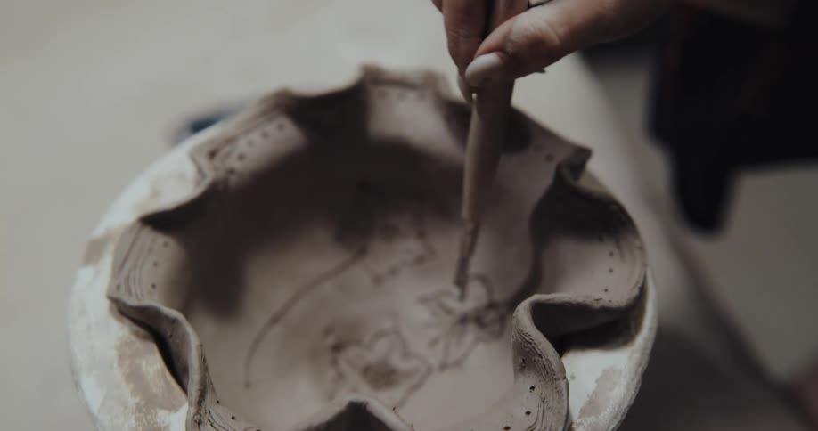 A woman uses a tool to carve in clay