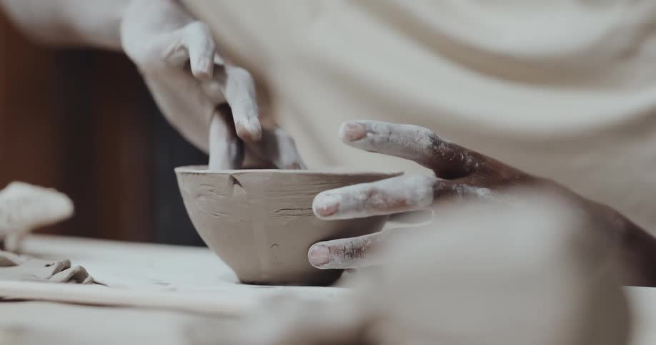 Young man crafting a ceramic bowl using his hands to smooth the edges
