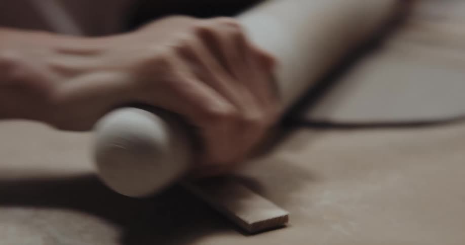 Woman uses rolling pin to roll out clay circle