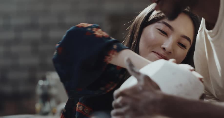 A man and woman flip a bowl with clay in it