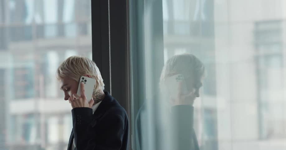 Excited blonde female with pixie haircut talking on cell phone near office window