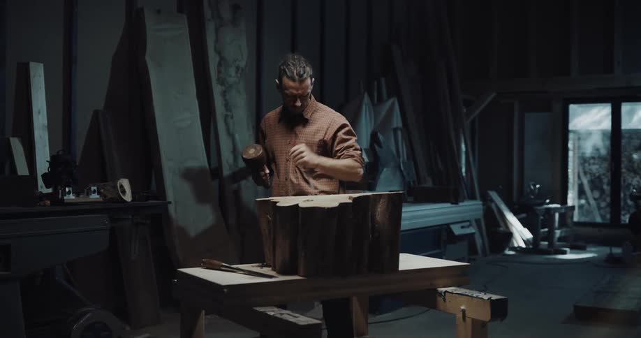 A man uses a chisel and mallet to start carving a wood stump
