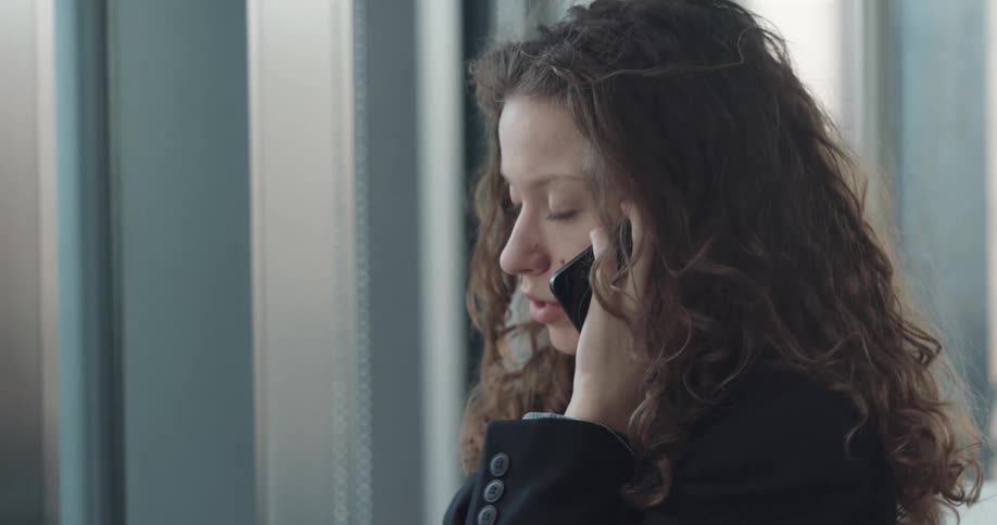A woman is standing by a window and talking on a cellphone