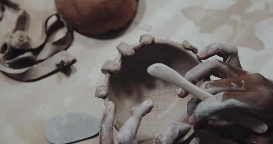 A woman uses a knife and her fingers to shape her clay sculpture of fingers holding a bowl