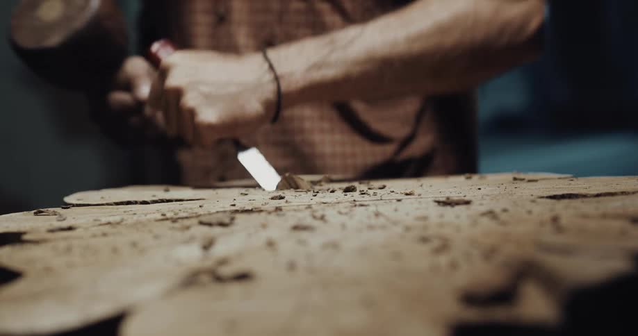A man uses a mallet and chisel to carve a tree trunk