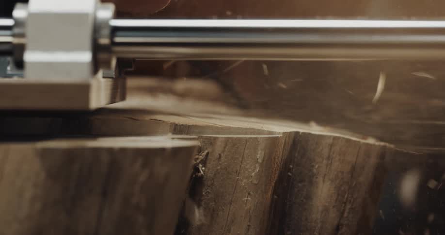 A planer is spewing sawdust as it smooths the top of a log