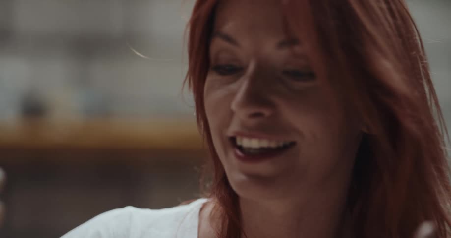 Redheaded woman pushes her hair back and talks while she forms clay bowl on potters wheel