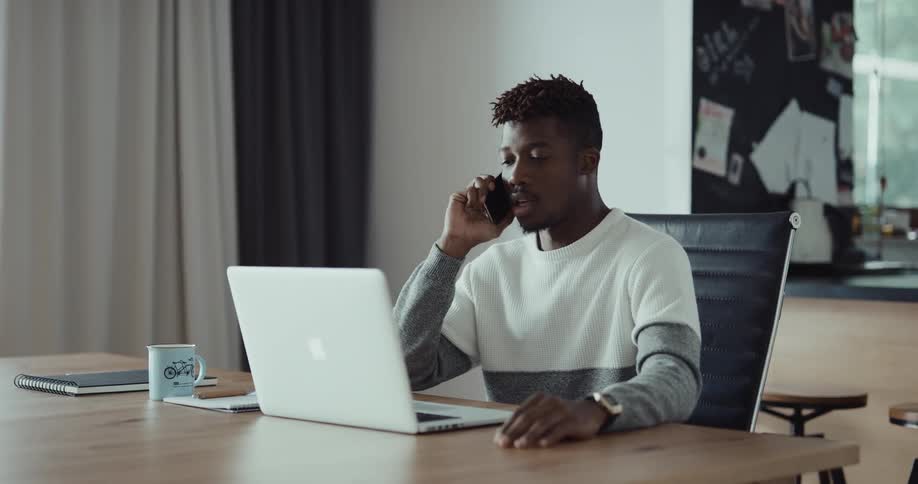 A man is talking on his cellphone and sitting at his desk