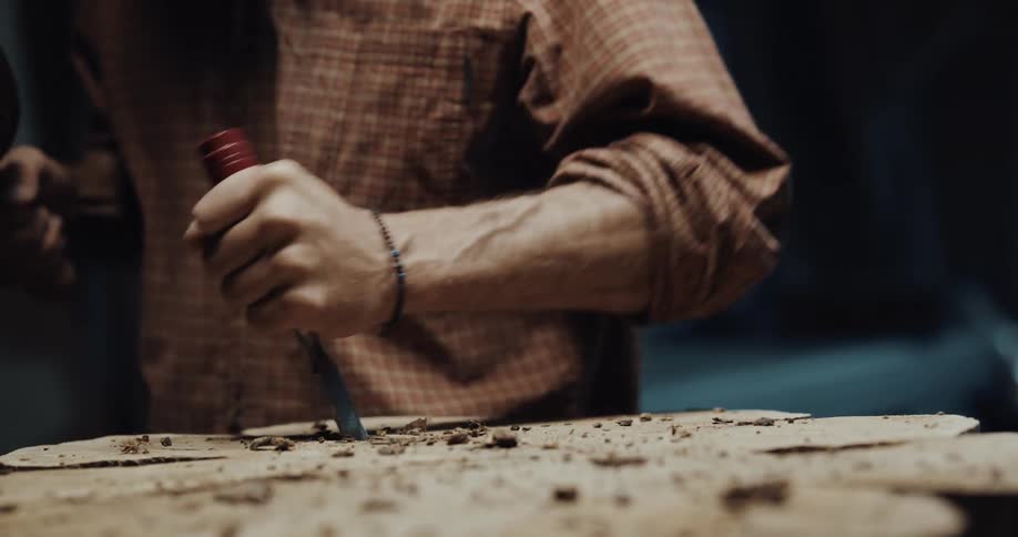 A man uses a mallet and chisel to carve a tree stump