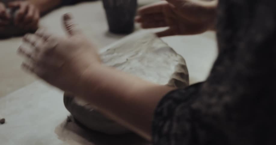 People sit around table conditioning clay by patting all the sides