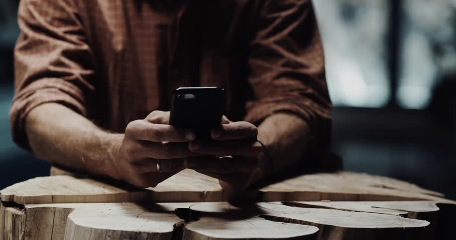 A man is standing indoors and texting on his cellphone