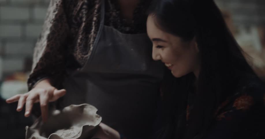 Student shows a freshly made clay bowl to a teacher inside a pottery workshop
