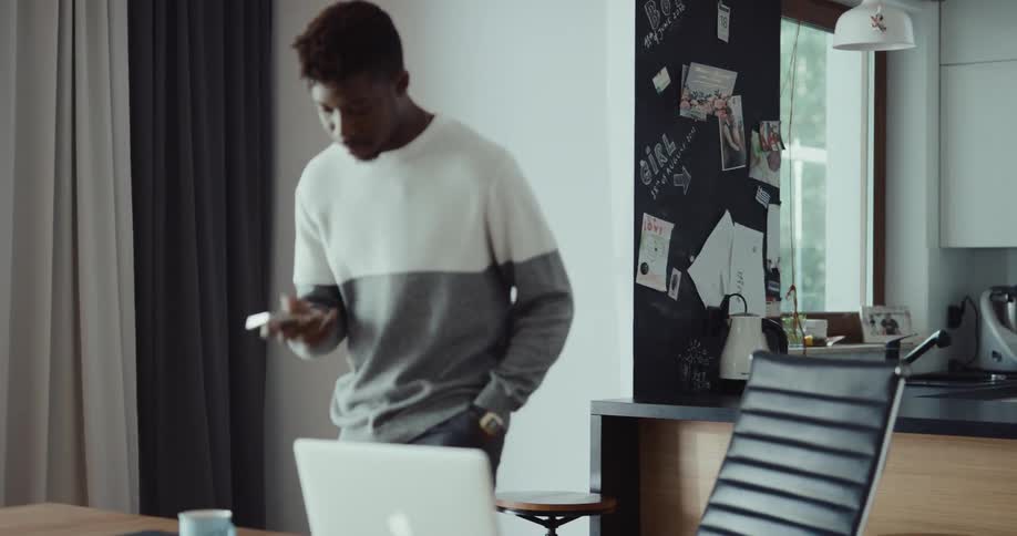 Man talks on phone near home office before sitting down in front of laptop
