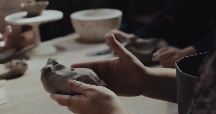 Teacher explaining how to shape a lump of fresh clay to a student