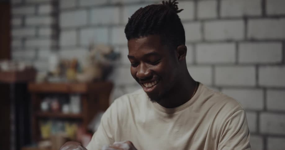 A man is making pottery and sitting indoors