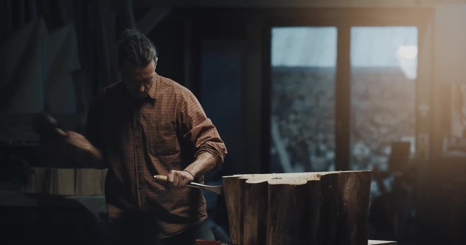 A man uses a large mallet and chisel to cut into a large piece of wood