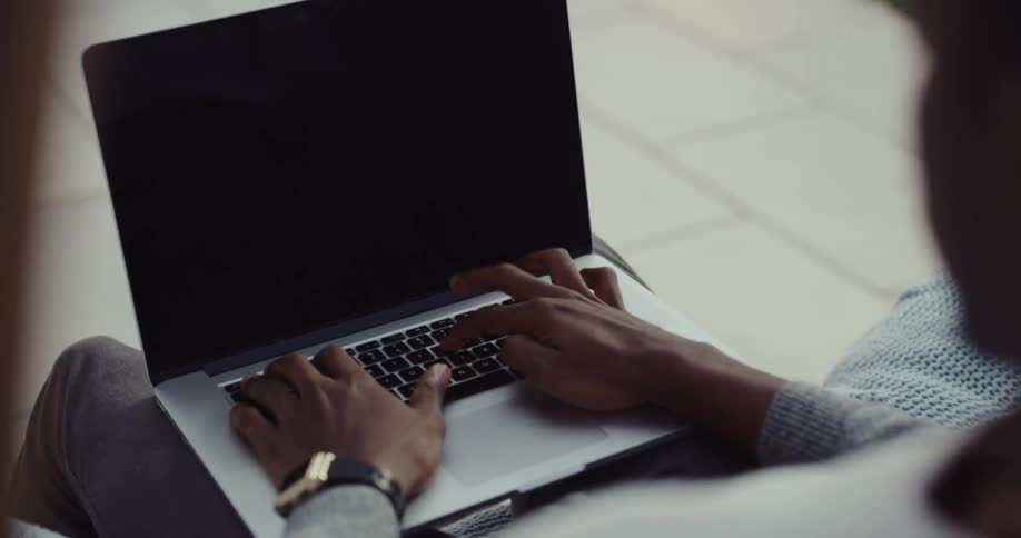A man is sitting outdoors with his laptop
