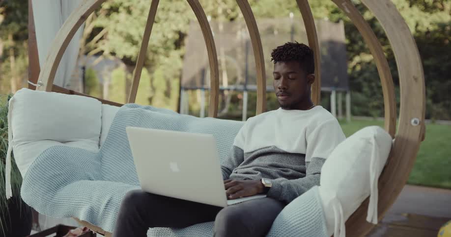 A man is sitting outdoors and browsing on his laptop