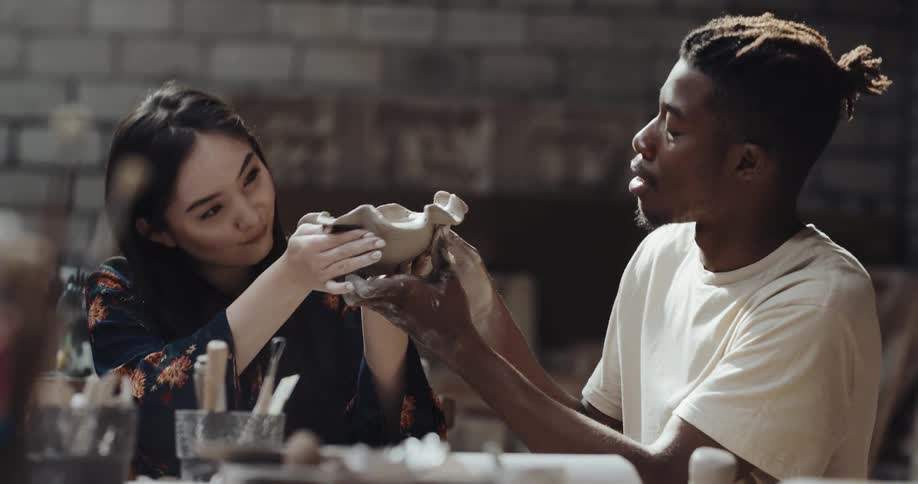Man and woman work on shaping clay bowl in studio