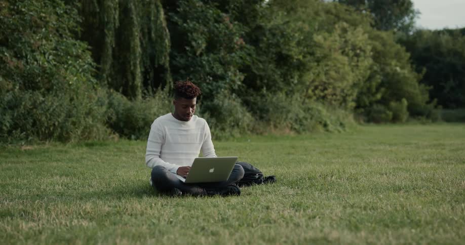 Man sits outdoors in field typing on laptop
