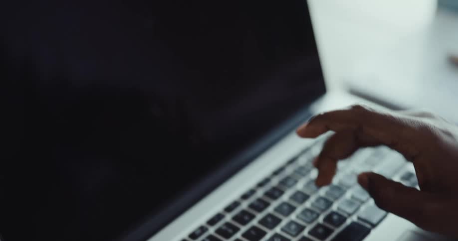 Black mans hands typing on a laptop in a wooden desk