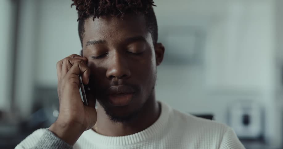 Man with white sweater and necklace answers phone in the kitchen