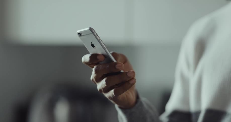 A man is standing indoors and texting on his cellphone