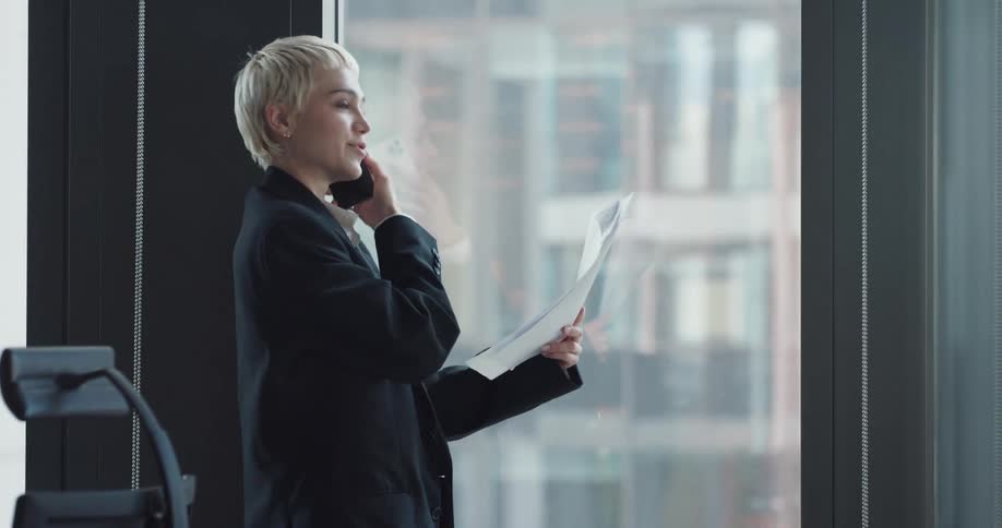 Businesswoman with naval blue blazer jacket and white shirt talks on smartphone at the office