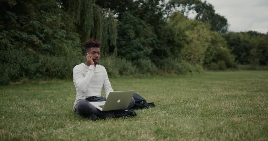 A man is typing on his laptop and sitting outdoors