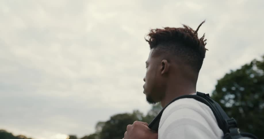 A man is walking outdoors and holding a backpack