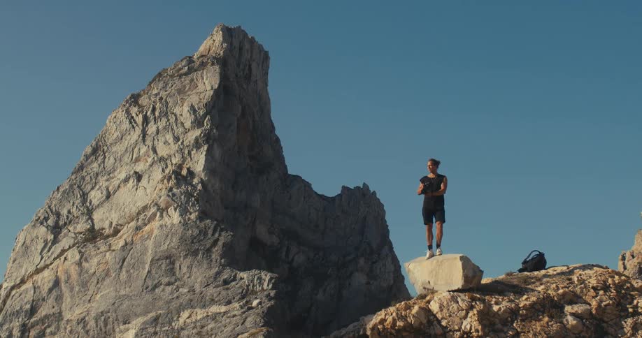 A photographer stands up on a rock high on a cliff and takes a photograph