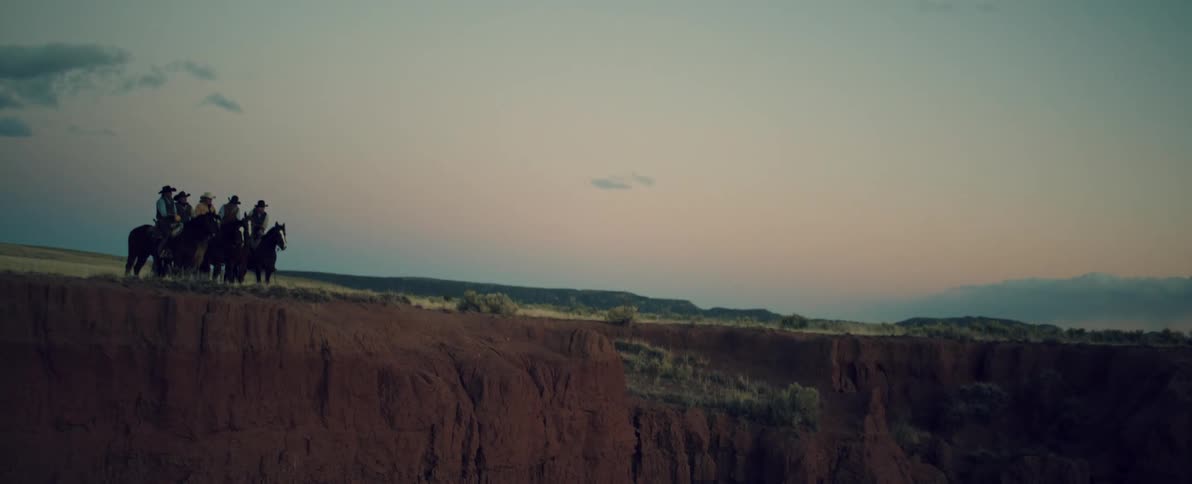 Aerial view of a group of cowboys on horseback standing near the edge of a cliff at evening