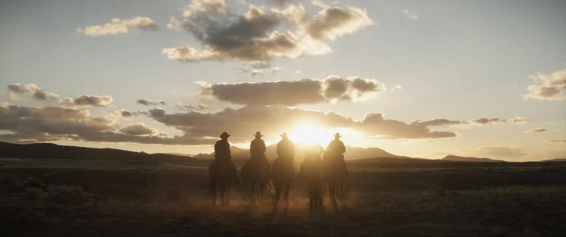 A group of men are riding horses in a rural area at dusk
