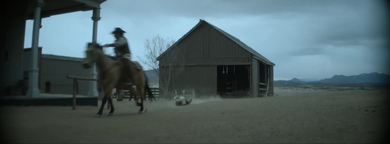 A man uses a rope to drag another man behind his horse while riding through an old western town