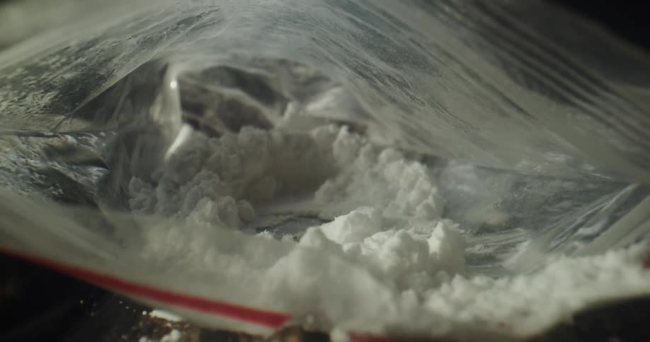 Clumps of white powder in small plastic bags with powder spilled out onto a table