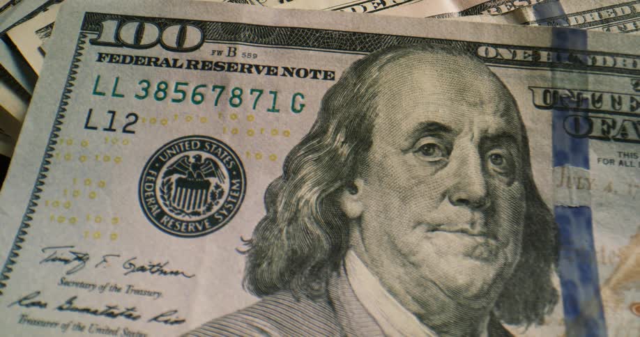 A stack of american banknotes fall onto a black surface