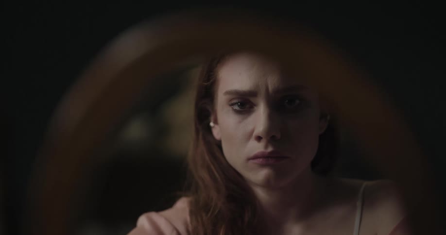 Distressed young redhead woman looking at herself in a round mirror