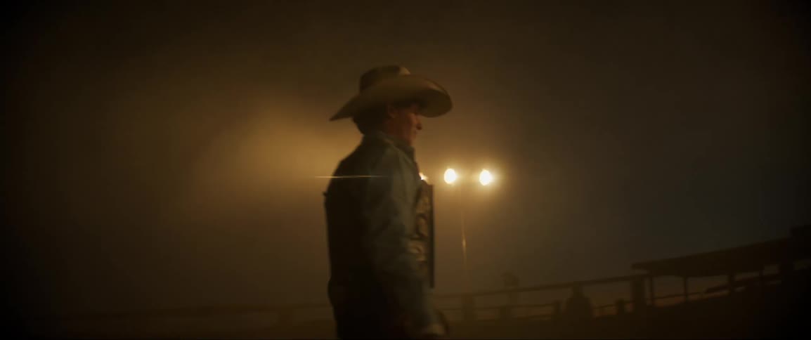 Cowboy walks across arena on foggy night lit by stadium lights
