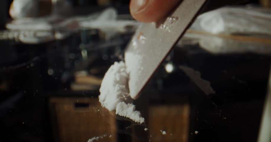 A person cuts lines of cocaine over a mirror using a credit card