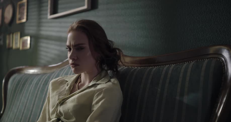 Young fancy beautiful woman sitting on the couch with an angry and suspicious facial expression