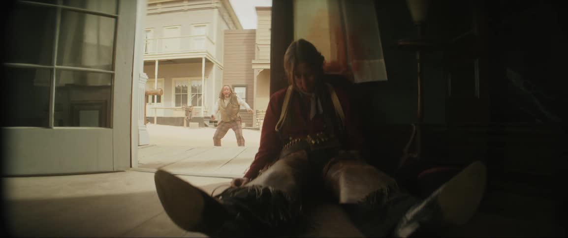 A man runs scared out a door past a dead man on the floor in the old west