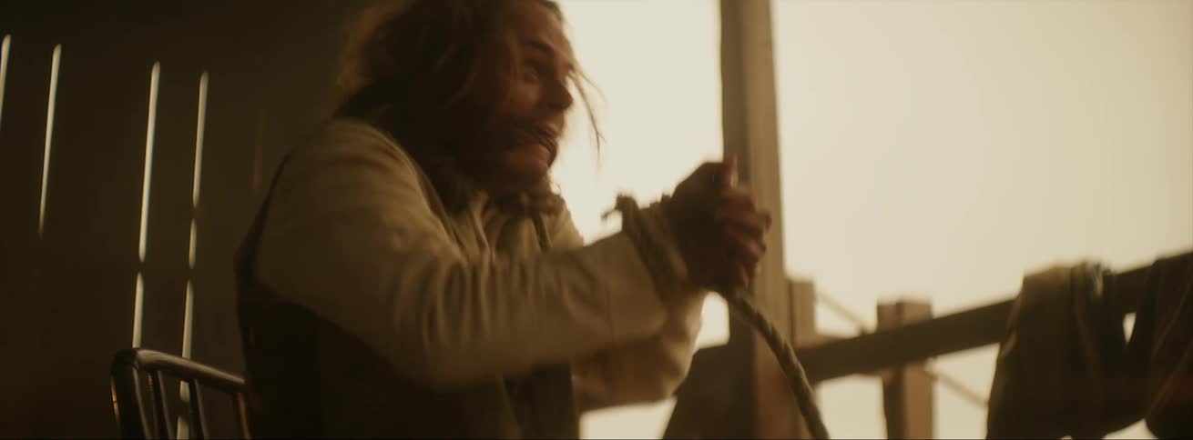 A man gagged with his hands tied in front of him begins to yell and strain against the ropes