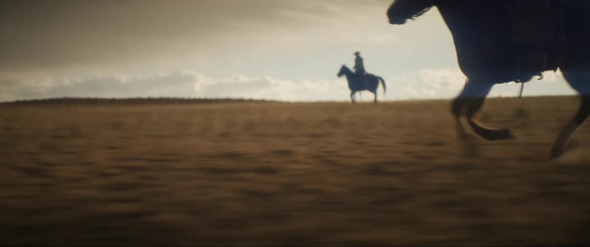 Silhouette of a group of cowboys galloping on horses through the plains at evening