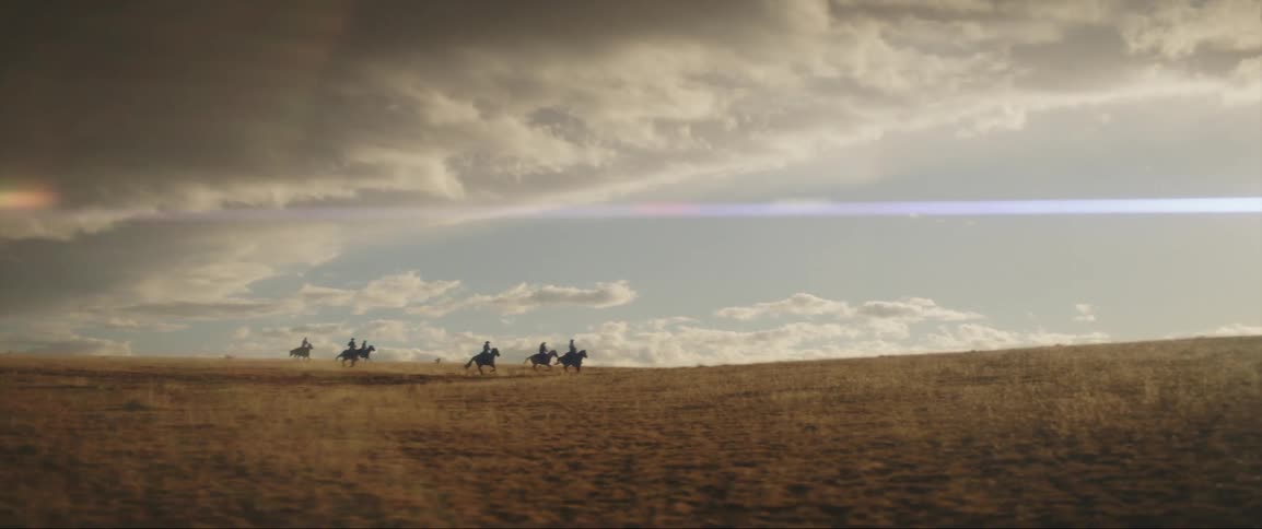 Six men riding horses on an open grass field on a sunny day