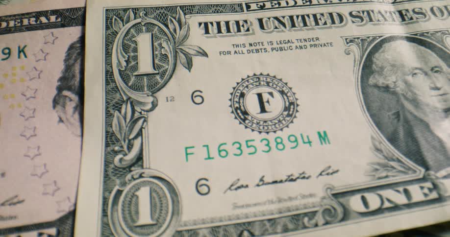 American banknotes fall onto a dark surface one by one