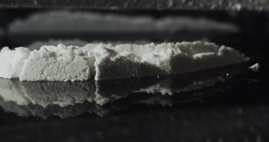 Extreme close up of a person cutting lines of cocaine using a razor blade