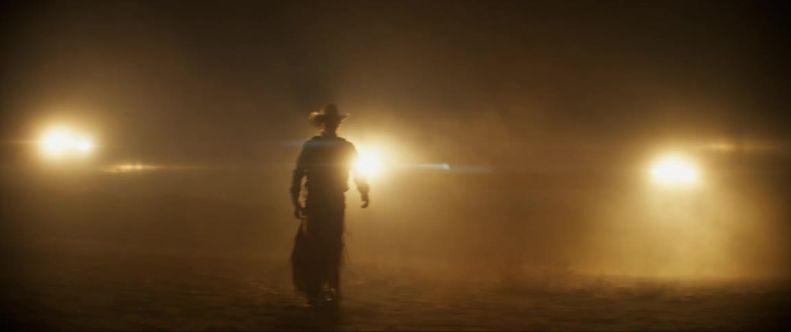 Silhouette of a cowboy walking away from bright spotlights at night