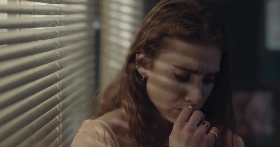 A woman is standing by a window and looks sad