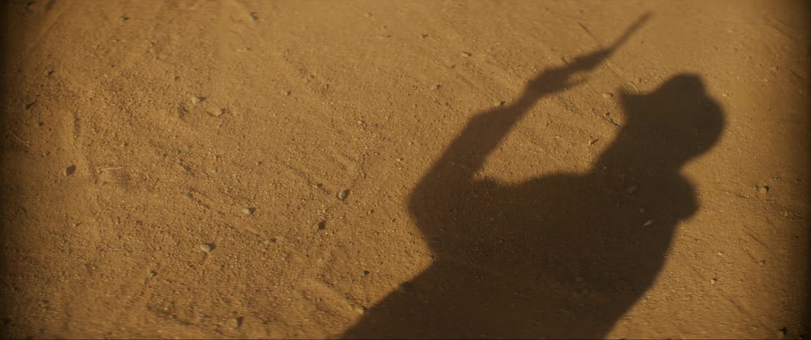 Shadow on wall of man wearing cowboy hat shooting a pistol